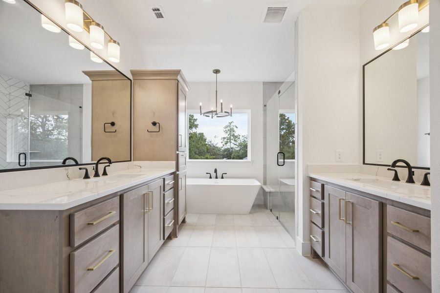 Luxurious primary bath with dual vanities, Omega Stone Quartz counters, framed mirrors, frameless-glass shower and a sleek soaking tub Luxurious primary bath with dual vanities, Omega Stone Quartz counters, framed mirrors, frameless-glass shower and a sleek soaking tub