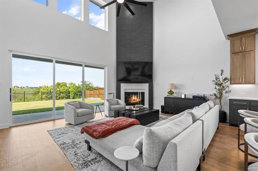Living room with wood finished floors, a fireplace, a towering ceiling, and ceiling fan Living room with wood finished floors, a fireplace, a towering ceiling, and ceiling fan