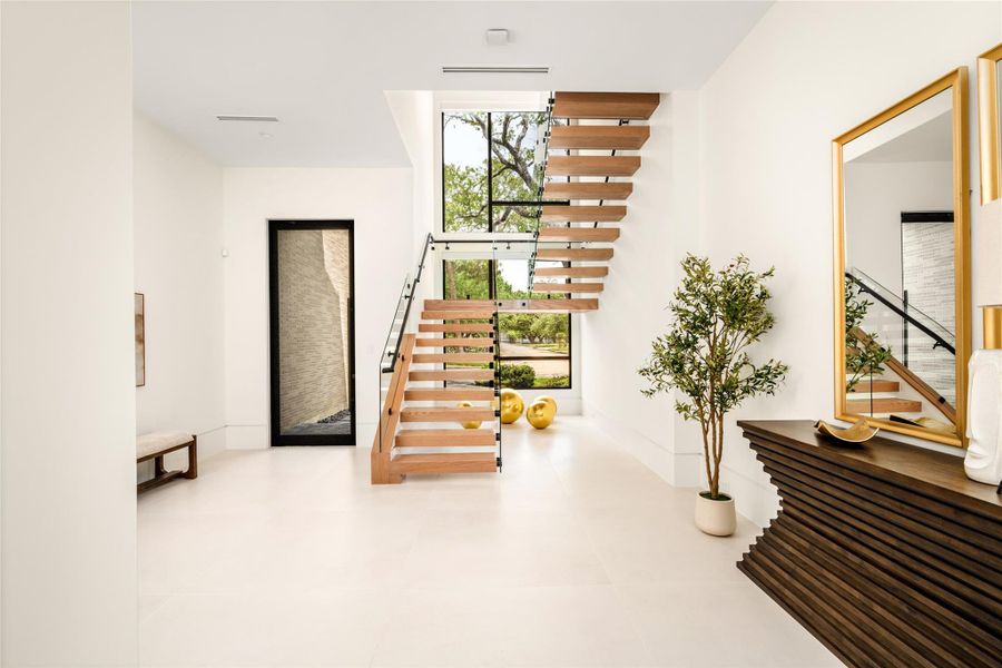 A dramatic entry foyer featuring a floating staircase, soaring ceilings, and expansive windows that fill the space with natural light.