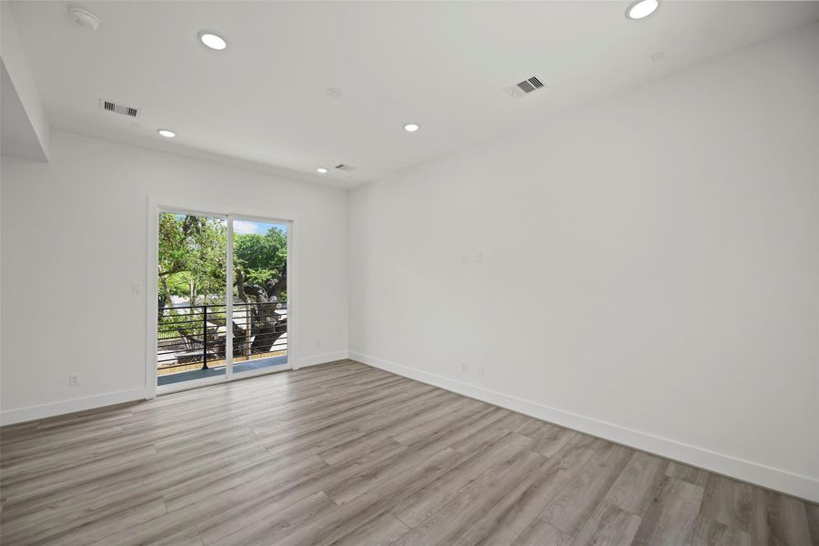 The living area features modern LVP flooring, recessed lighting, and a large sliding glass door leading to a balcony with a view of lush greenery, creating a bright and inviting space.