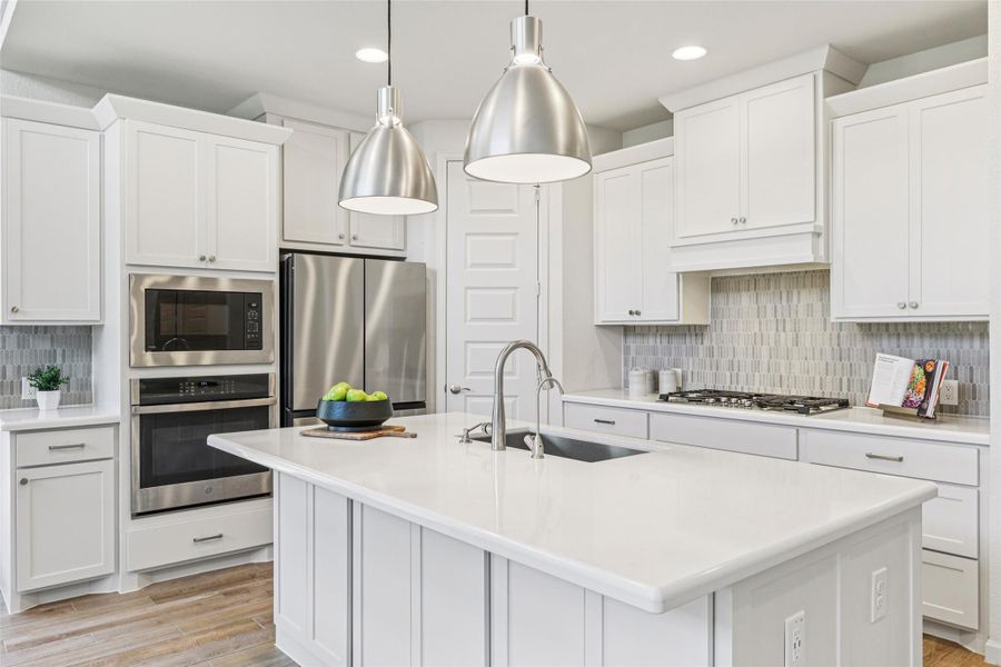 Modern kitchen featuring white cabinetry, stainless steel appliances, a center island with a sink, and pendant lighting