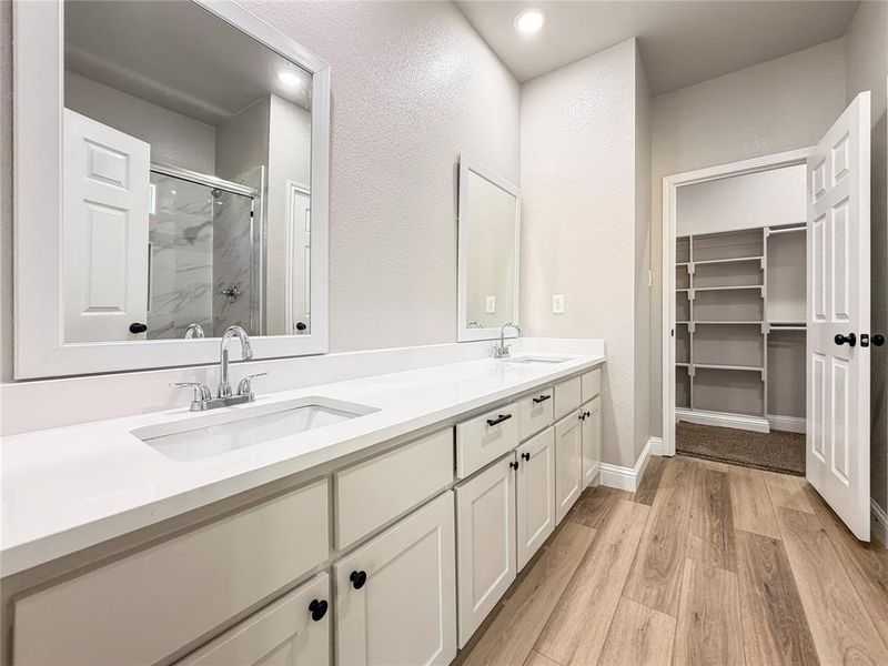 Bathroom with a marble finish shower, double vanity, light wood-style floors, a walk in closet, and recessed lighting Bathroom with a marble finish shower, double vanity, light wood-style floors, a walk in closet, and recessed lighting