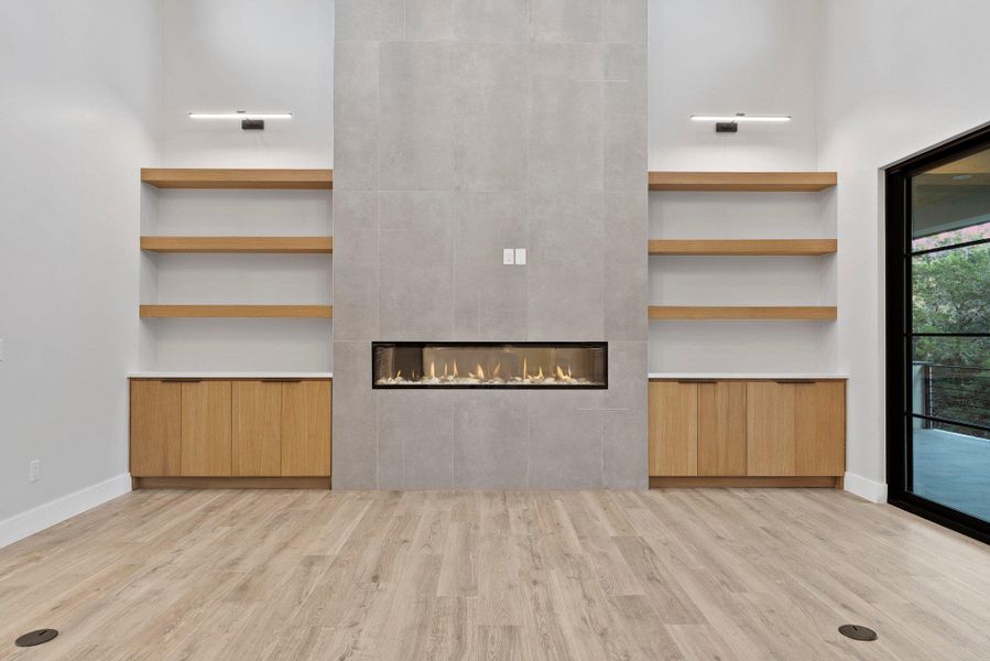 A modern living space features a linear fireplace, flanked by custom cabinetry and floating shelves, all set against neutral tones.