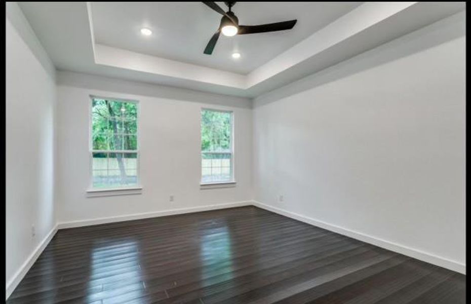 Empty room featuring dark wood-type flooring, ceiling fan, and a tray ceiling