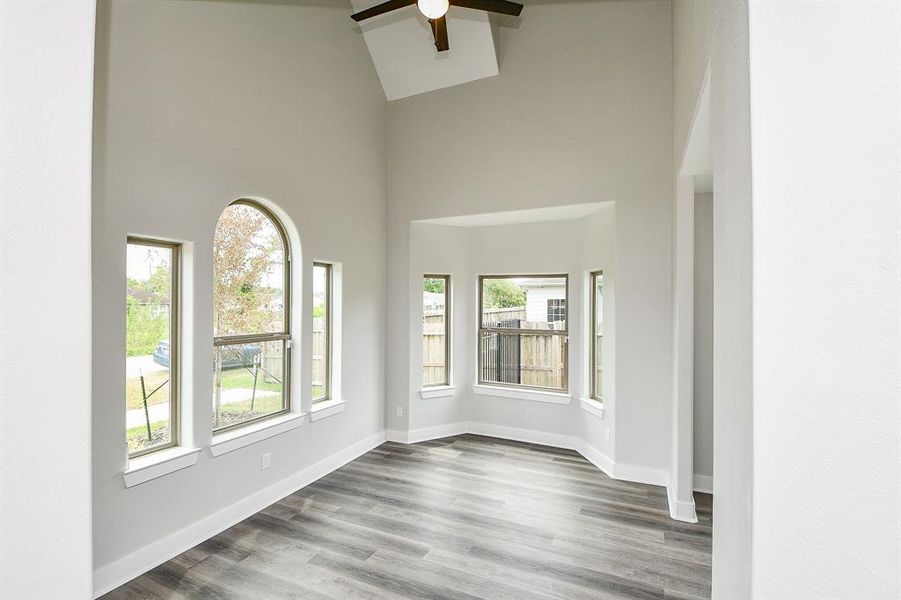 Another view of this  bright, and spacious  living room with high vaulted ceilings, a ceiling fan, arched and rectangular windows allowing for natural light, and modern grey-toned flooring.