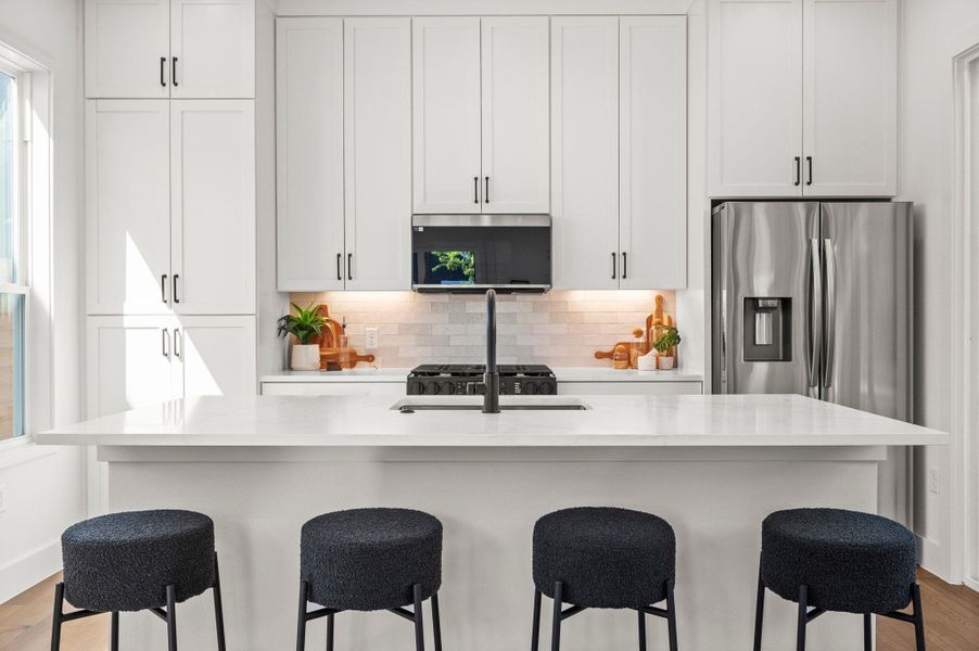 Kitchen with light wood-style flooring, tasteful backsplash, white cabinets, stainless steel microwave, and light stone counters Kitchen with light wood-style flooring, tasteful backsplash, white cabinets, stainless steel microwave, and light stone counters