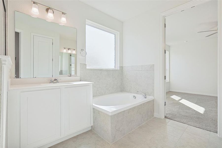 Bathroom with vanity, a relaxing tiled tub, ceiling fan, and tile patterned flooring