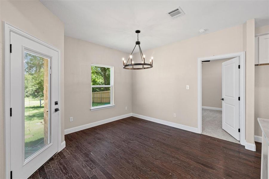 Spacious room featuring dark wood-finish flooring, light neutral-toned walls, and a contemporary black chandelier
