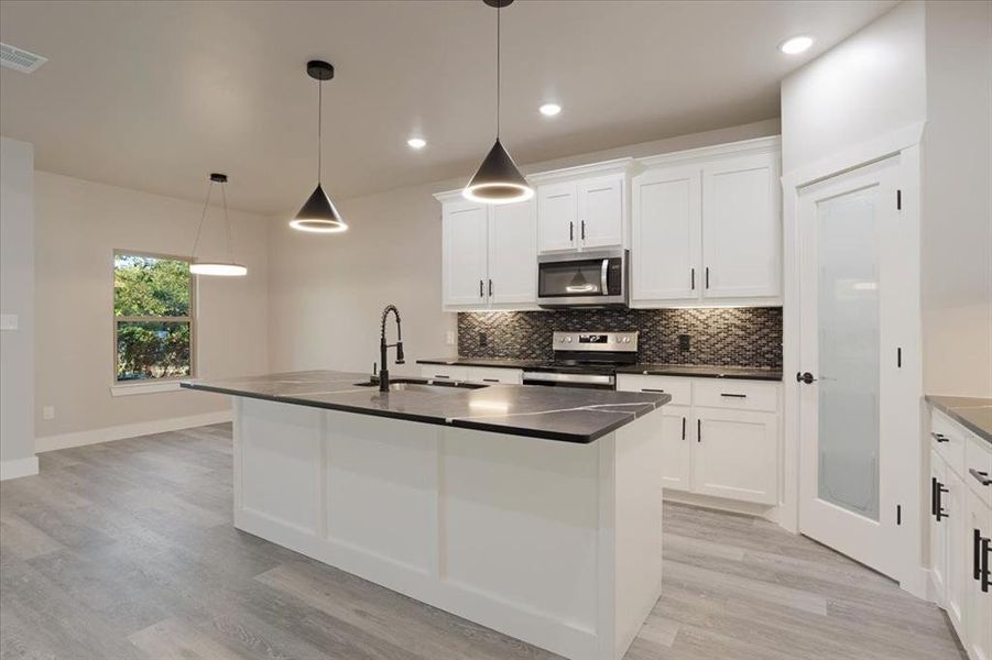 Kitchen with an island with sink, white cabinetry, pendant lighting, light hardwood / wood-style floors, and stainless steel appliances