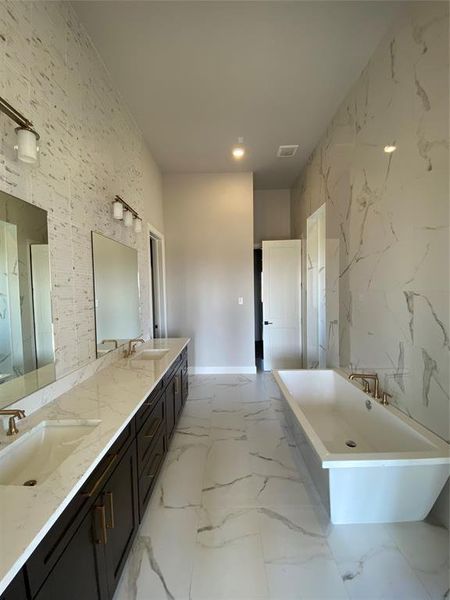 Bathroom featuring tile walls, light marble finish flooring, double vanity, stone wall, and a freestanding tub