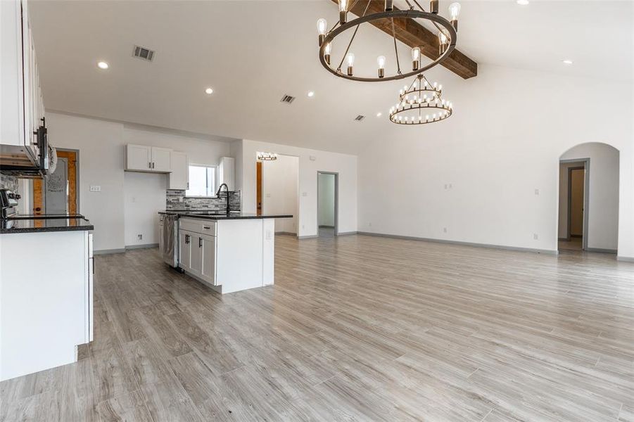 Kitchen with light hardwood / wood-style flooring, a chandelier, white cabinetry, a center island with sink, and vaulted ceiling with beams