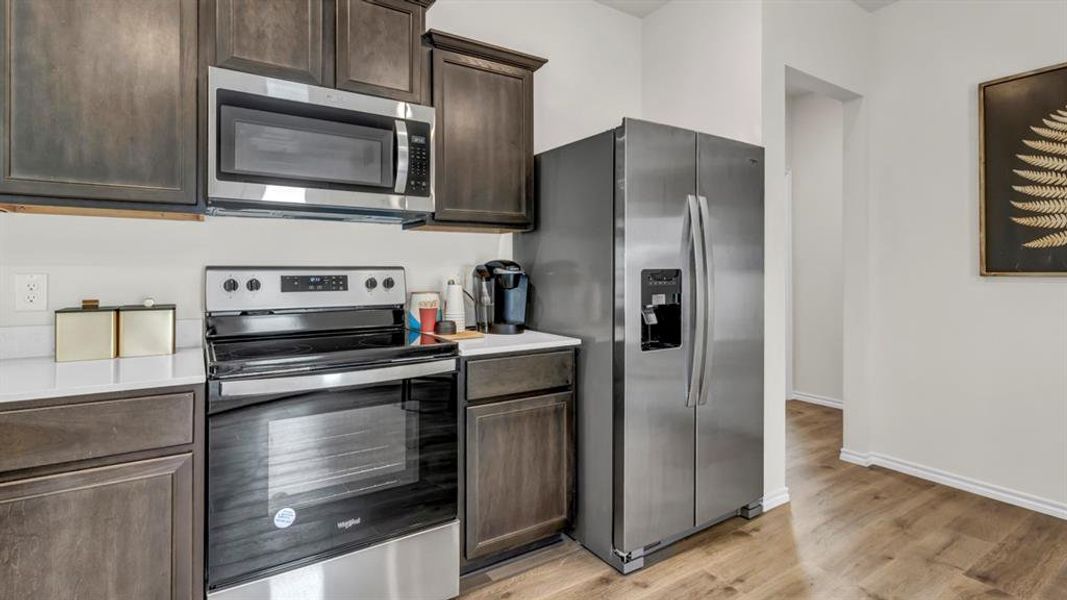 Kitchen featuring stainless steel appliances, dark wood finish cabinets, and light wood-type flooring Kitchen featuring stainless steel appliances, dark wood finish cabinets, and light wood-type flooring