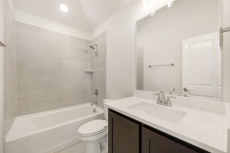 Bathroom with tiled tub-shower combo, dark vanity with quartz countertop, and large mirror