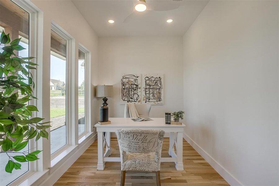 Home office featuring light wood-type flooring, ceiling fan, and a healthy amount of sunlight