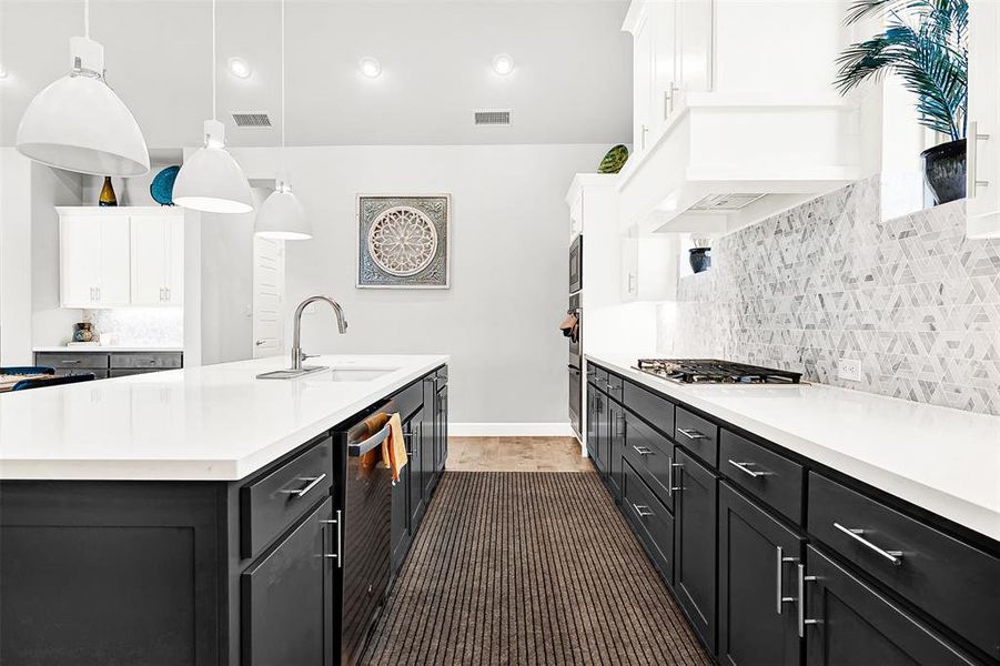 Kitchen featuring tasteful backsplash, dark cabinets, hanging light fixtures, a kitchen island with sink, and white cabinetry