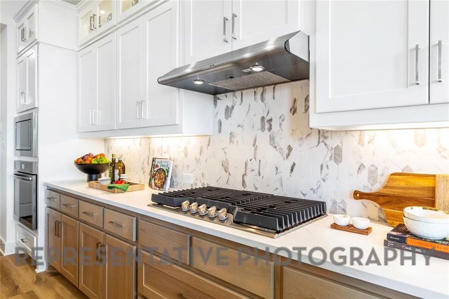 Kitchen with white cabinetry, under cabinet range hood, tasteful backsplash, and appliances with stainless steel finishes Kitchen with white cabinetry, under cabinet range hood, tasteful backsplash, and appliances with stainless steel finishes
