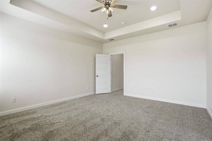 Spacious room featuring neutral carpeting, white walls, a tray ceiling, recessed lighting, and a ceiling fan