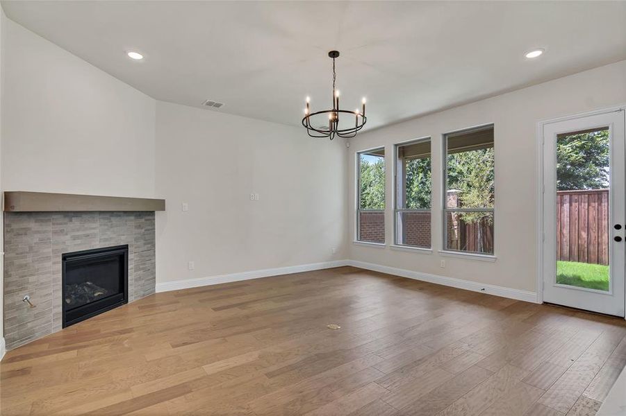 Unfurnished living room with plenty of natural light, a tiled fireplace, a chandelier, and light hardwood / wood-style floors