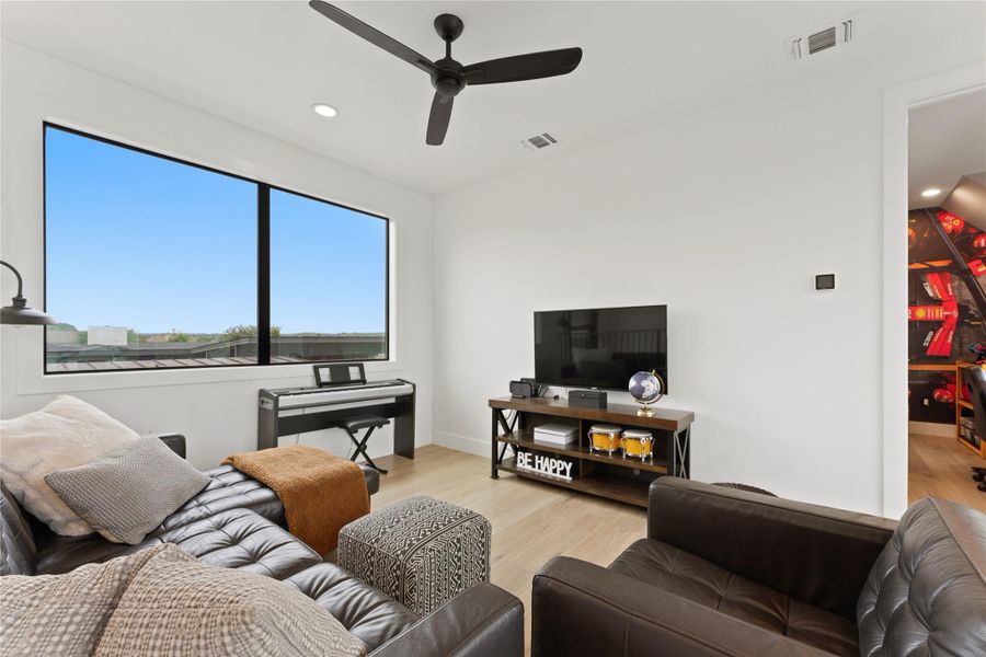 Bright room featuring a large horizontal window, light wood-finish flooring, a contemporary black ceiling fan with recessed lighting, white walls, and an open doorway Bright room featuring a large horizontal window, light wood-finish flooring, a contemporary black ceiling fan with recessed lighting, white walls, and an open doorway