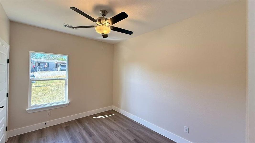 Interior room featuring wood-finish flooring, light neutral-toned walls, and a ceiling fan with integrated lighting Interior room featuring wood-finish flooring, light neutral-toned walls, and a ceiling fan with integrated lighting