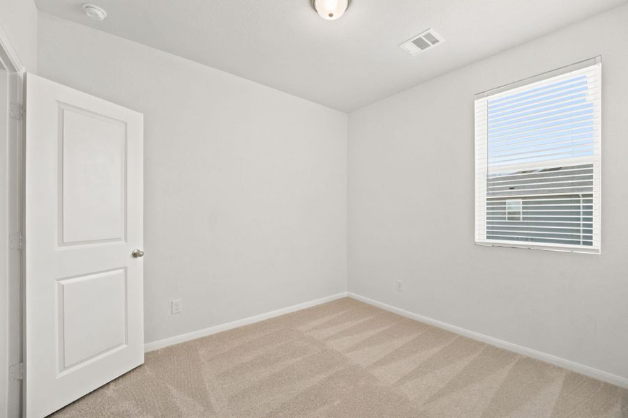 Soft carpeting pairs with a bright window inside this versatile secondary bedroom space.