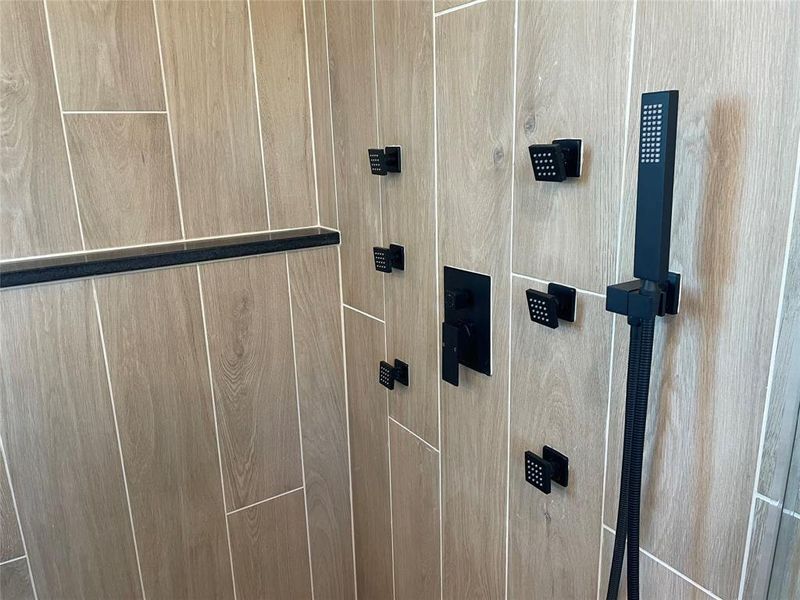 Shower featuring wood-finish tile walls, a matte black shower panel with multiple body sprays, and a handheld showerhead
