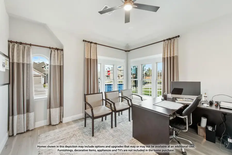 Home office with dark wood desk, ceiling fan, vaulted ceiling, and large windows with neutral curtains Home office with dark wood desk, ceiling fan, vaulted ceiling, and large windows with neutral curtains