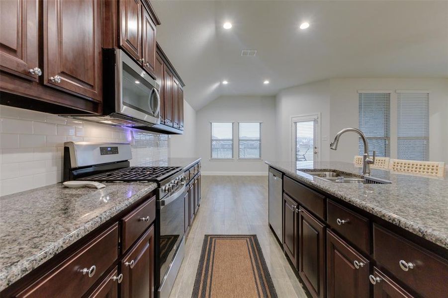 Kitchen with sink, light wood-type flooring, tasteful backsplash, dark brown cabinetry, and stainless steel appliances