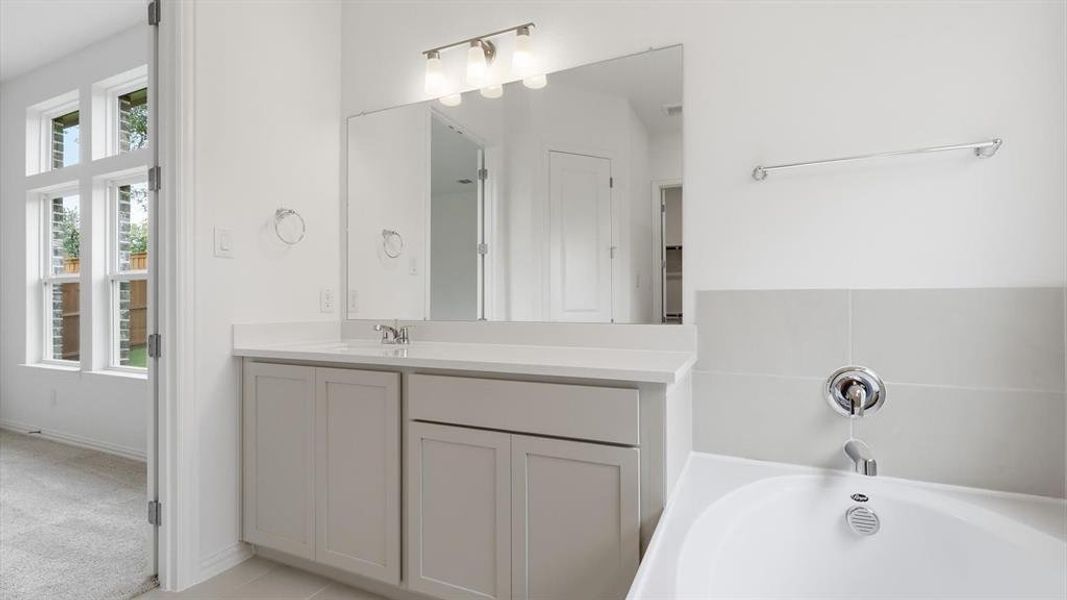 Bathroom featuring a light gray vanity with a single sink, an integrated bathtub, and large windows Bathroom featuring a light gray vanity with a single sink, an integrated bathtub, and large windows