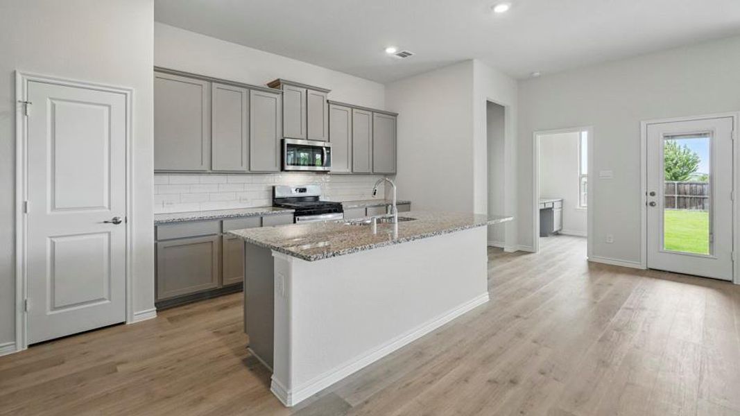 The kitchen features light grey cabinetry, a white subway tile backsplash, and granite countertops