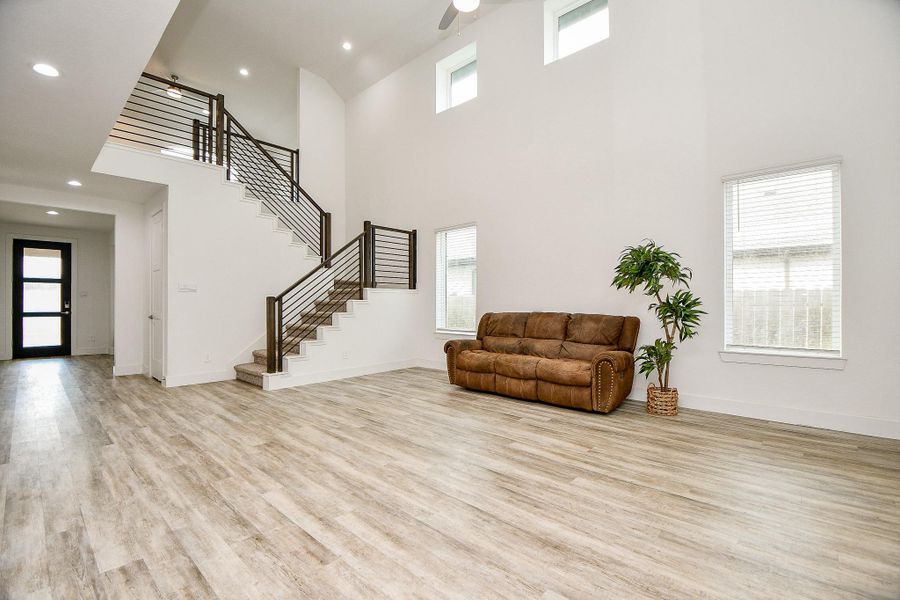 This spacious living area features high ceilings and ample natural light from large windows. The modern staircase with sleek horizontal iron railing adds a contemporary touch, while the vinyl plank flooring complements the open, airy feel. This spacious living area features high ceilings and ample natural light from large windows. The modern staircase with sleek horizontal iron railing adds a contemporary touch, while the vinyl plank flooring complements the open, airy feel.