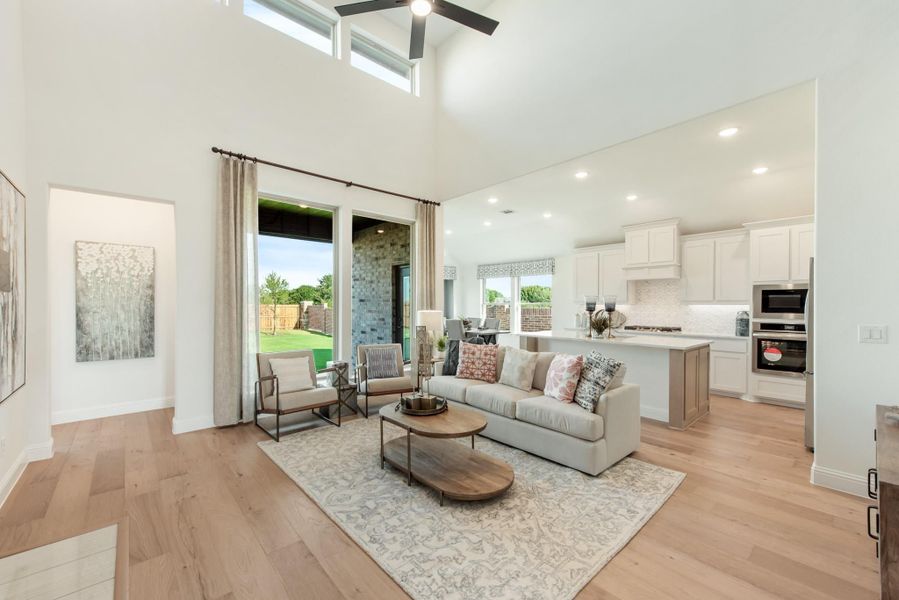 Open-concept living room with high ceilings, hardwood floors, and kitchen visible in background Open-concept living room with high ceilings, hardwood floors, and kitchen visible in background