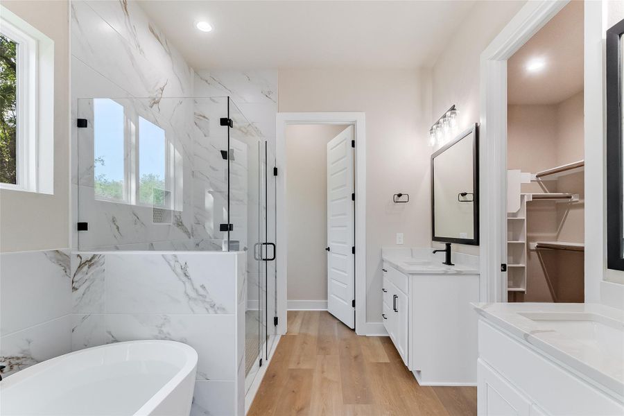 Bathroom with a marble finish shower, vanity, a freestanding tub, light wood-style flooring, and two sinks Bathroom with a marble finish shower, vanity, a freestanding tub, light wood-style flooring, and two sinks