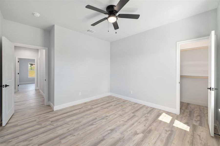 Unfurnished bedroom featuring a walk in closet, ceiling fan, light wood finished floors, baseboards, and visible vents