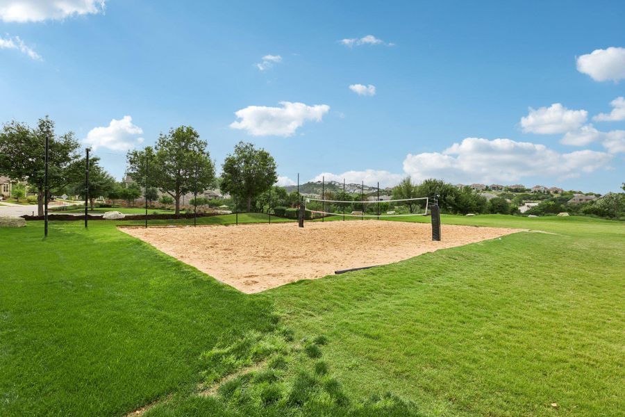 Outdoor sand volleyball court with a net, surrounded by a manicured lawn and mature trees