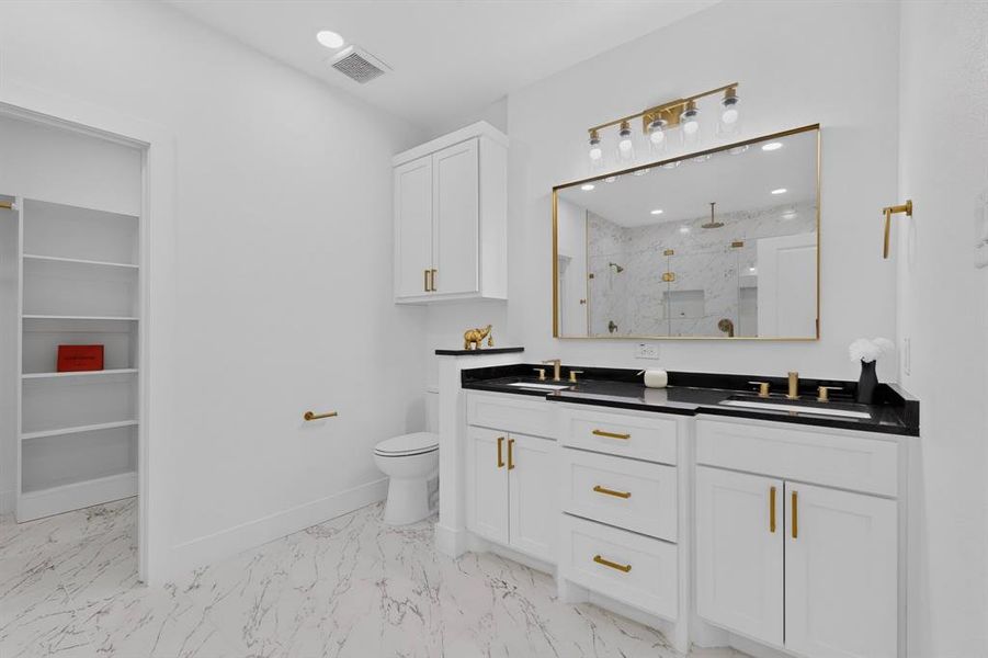Bathroom featuring a dual vanity with black countertops, white cabinetry, and gold-finish hardware