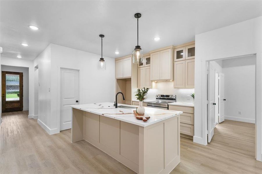 Modern kitchen featuring a central island with a light-toned countertop, pendant lighting, and light wood-finish cabinetry Modern kitchen featuring a central island with a light-toned countertop, pendant lighting, and light wood-finish cabinetry