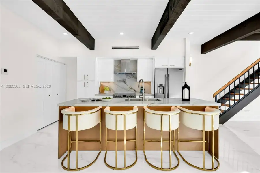 Kitchen featuring dark cedar wood-finish ceiling beams, white slim shaker-style cabinetry, stone-finish countertops, stainless steel appliances, and large-format tile flooring Kitchen featuring dark cedar wood-finish ceiling beams, white slim shaker-style cabinetry, stone-finish countertops, stainless steel appliances, and large-format tile flooring