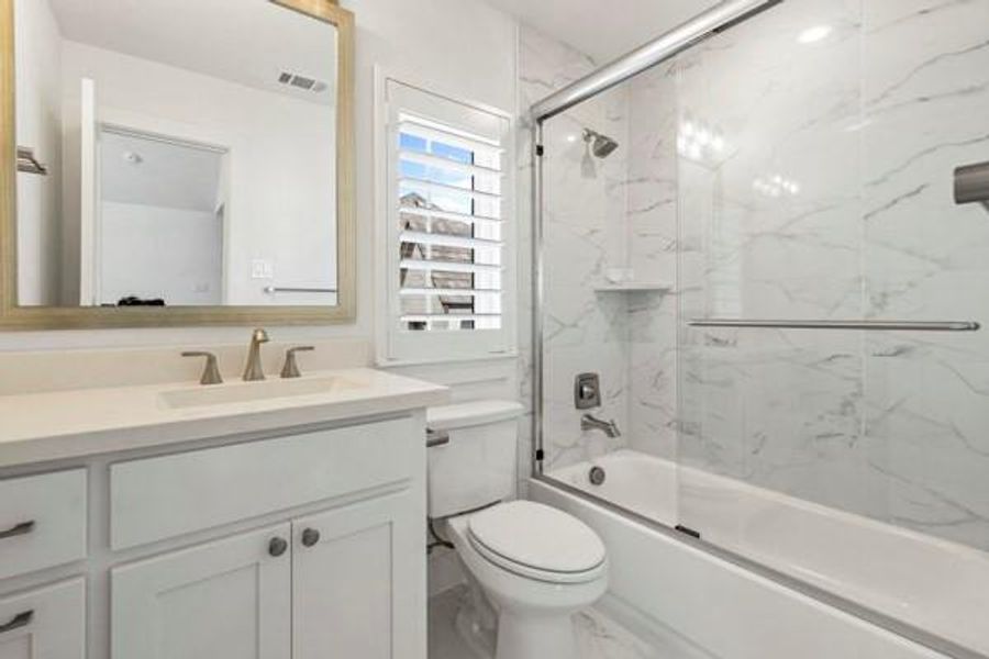 Bathroom featuring shower / bath combination with glass door, vanity, and marble look tiles Bathroom featuring shower / bath combination with glass door, vanity, and marble look tiles