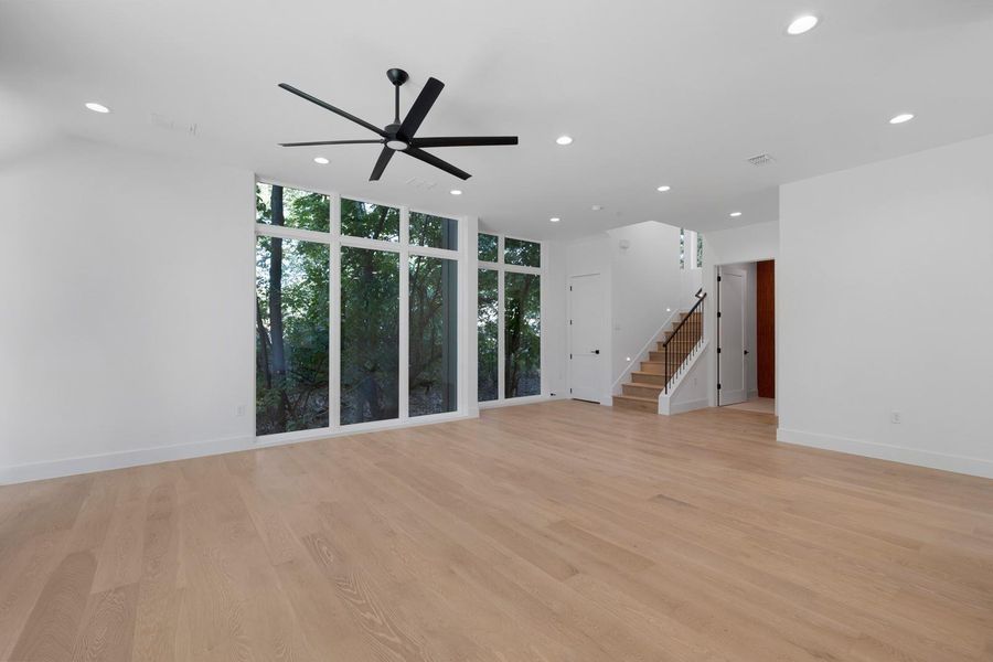 Unfurnished living room featuring expansive windows, recessed lighting, light wood finished floors, stairway, and a ceiling fan Unfurnished living room featuring expansive windows, recessed lighting, light wood finished floors, stairway, and a ceiling fan