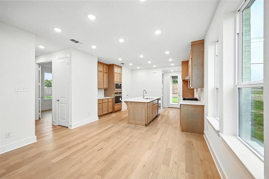 Kitchen featuring light wood finished floors, recessed lighting, an island with sink, appliances with stainless steel finishes, and decorative backsplash Kitchen featuring light wood finished floors, recessed lighting, an island with sink, appliances with stainless steel finishes, and decorative backsplash