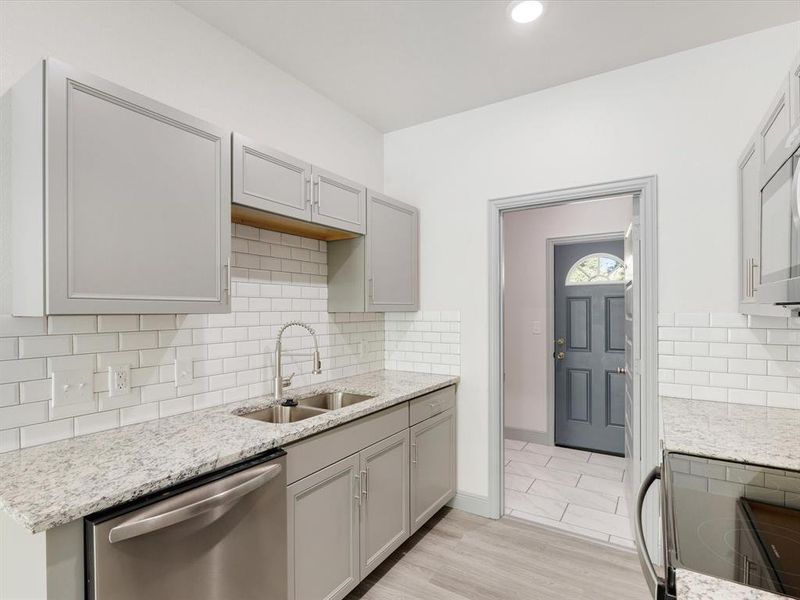 Kitchen with stainless steel appliances, gray cabinetry, backsplash, light stone countertops, and light wood finished floors