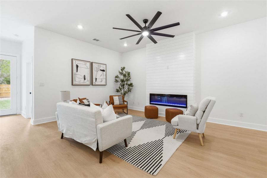 Living area with light wood-style floors, ceiling fan, a large fireplace, and recessed lighting