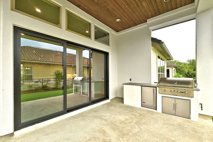 Covered patio featuring an outdoor kitchen with built-in grill, under-counter refrigerator, and stone-finish countertop