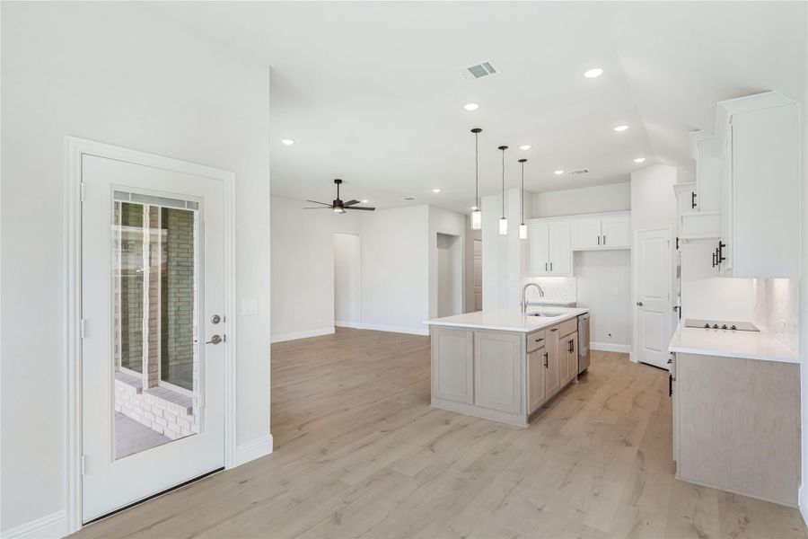 Open kitchen and living area with white cabinets, center island, pendant lights, and light wood floors