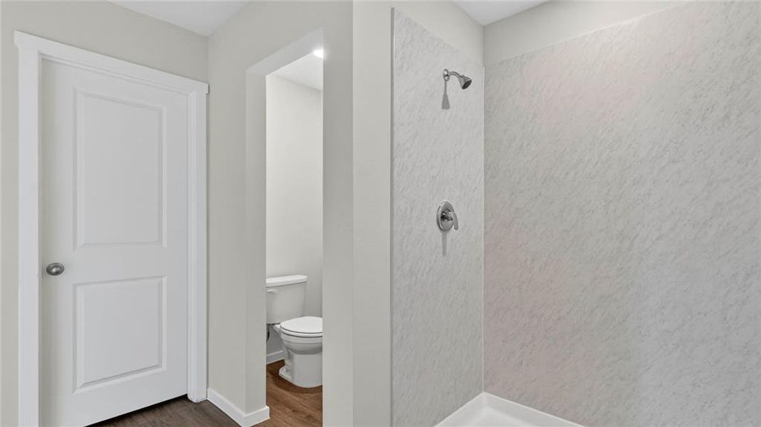 Shower enclosure featuring a chrome shower head and handle, with a separate water closet visible through an open doorway