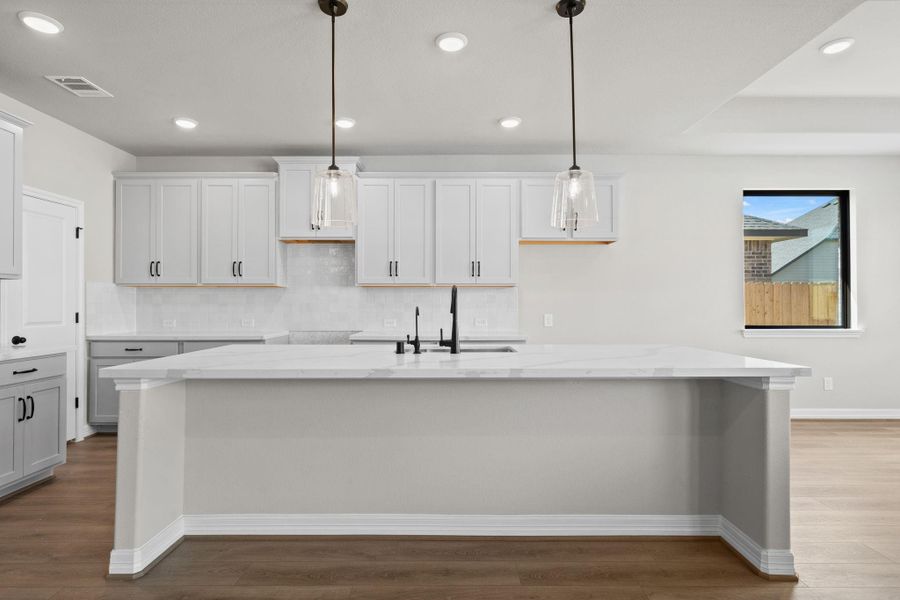 This light and bright kitchen features a large quartz island, white cabinets, a large sink overlooking your family room, recessed lighting, and beautiful backsplash.