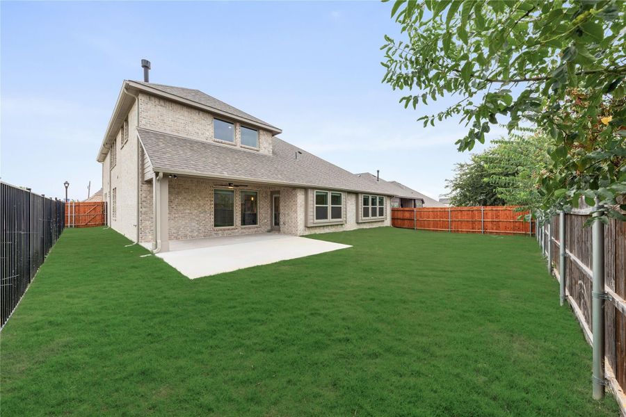 Two-story brick home with covered patio, concrete slab, and large fenced backyard with green lawn Two-story brick home with covered patio, concrete slab, and large fenced backyard with green lawn