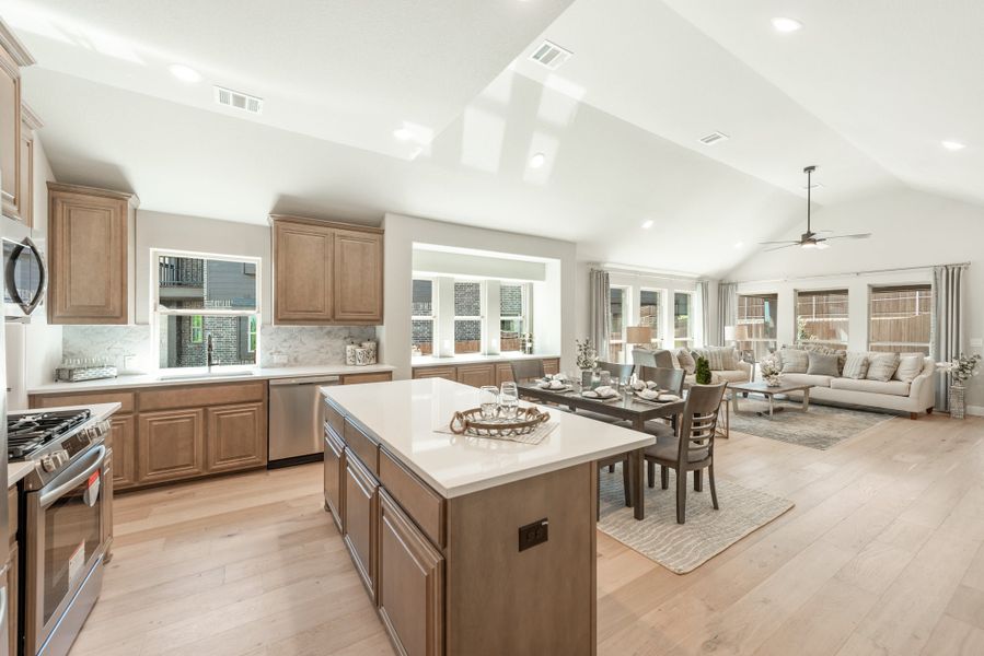 Open-concept kitchen with center island, wood cabinets, and vaulted ceiling flowing into dining and living areas