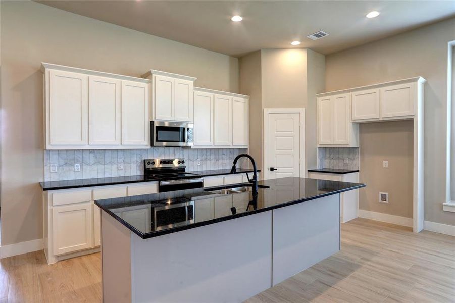 Kitchen featuring backsplash, white cabinetry, dark stone counters, a center island with sink, and appliances with stainless steel finishes Kitchen featuring backsplash, white cabinetry, dark stone counters, a center island with sink, and appliances with stainless steel finishes
